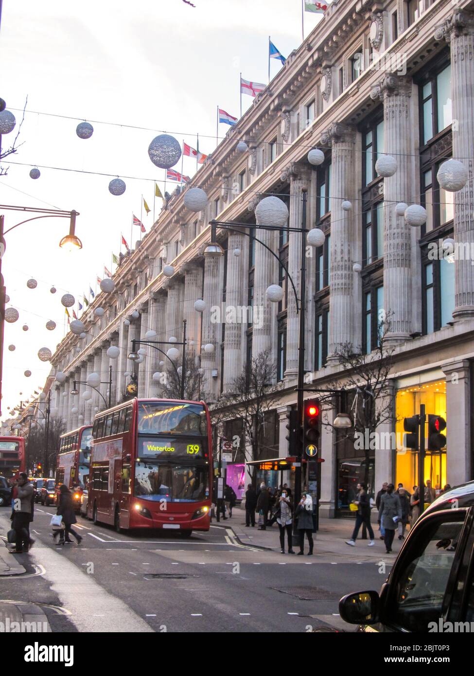 Red double decker busses in front of the Selfridge Department store on Oxford Street, London, with Christmas decorations stretched over the street Stock Photo