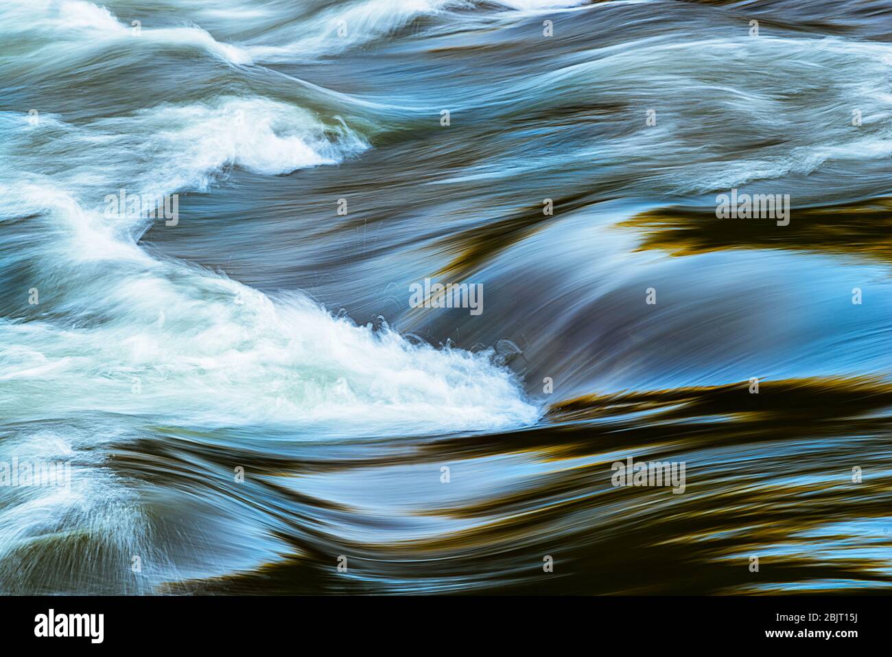 Blues, golds and greens reflect on the surface of the New River, creating the appearance of a molten mixture fusing together the substances of nature Stock Photo