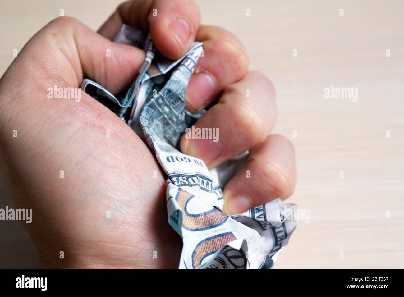 Hand squeezes hundred dollar bills on a light wooden table. side view. to close Stock Photo