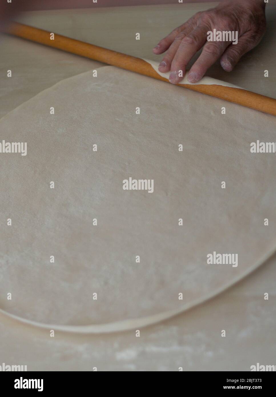 Hands baking dough with rolling pin on wooden table for turkish food manti. Manti is a type of dumpling popular in most Turkic cuisines Stock Photo