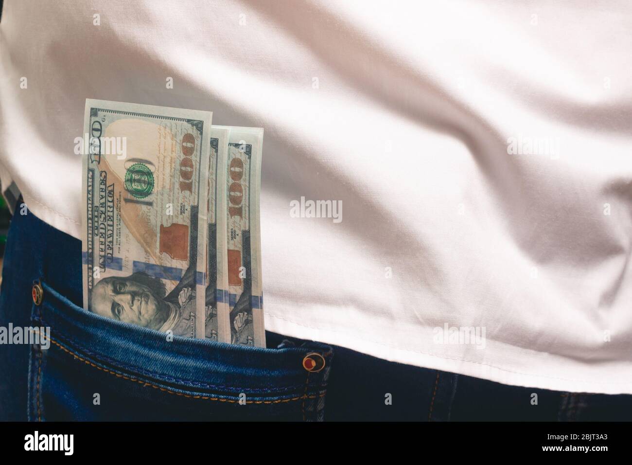 a man puts in his back pocket jeans a pack of hundred-dollar bills in a white shirt in the office Stock Photo