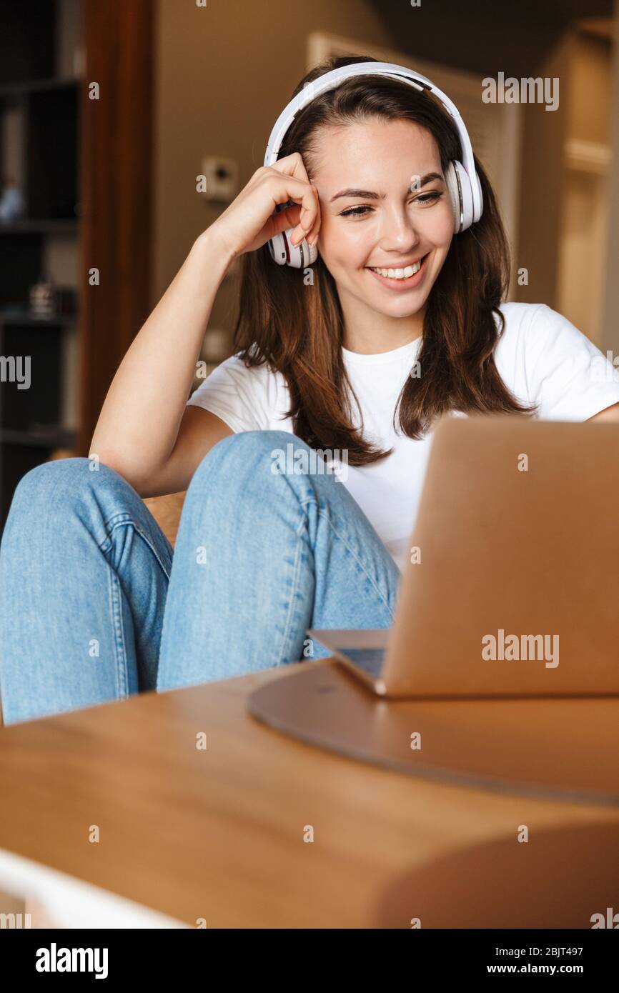 Photo of a beautiful young positive woman indoors at home using laptop ...