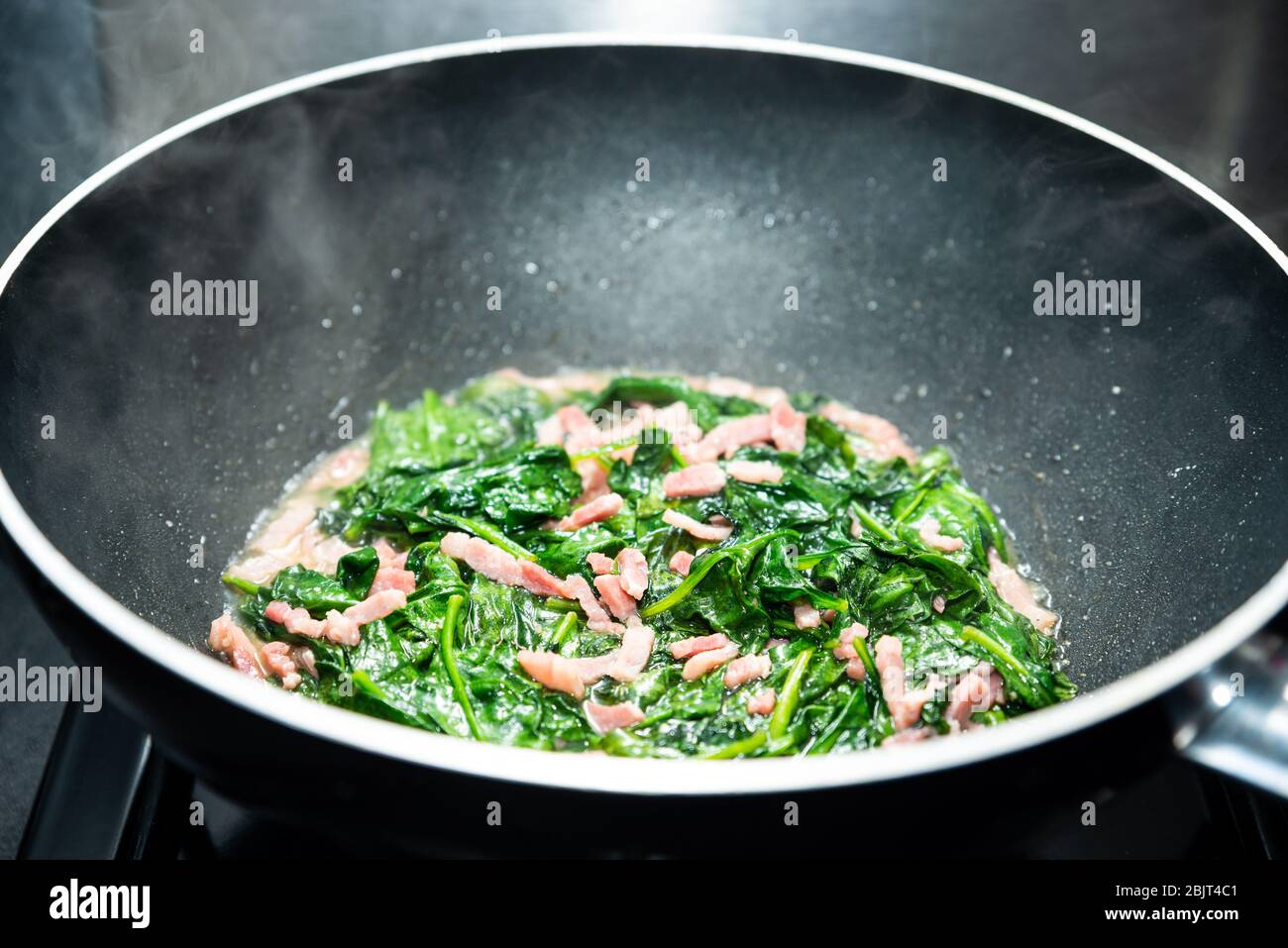 Cooking spinach with diced bacon in nonstick wok Stock Photo Alamy