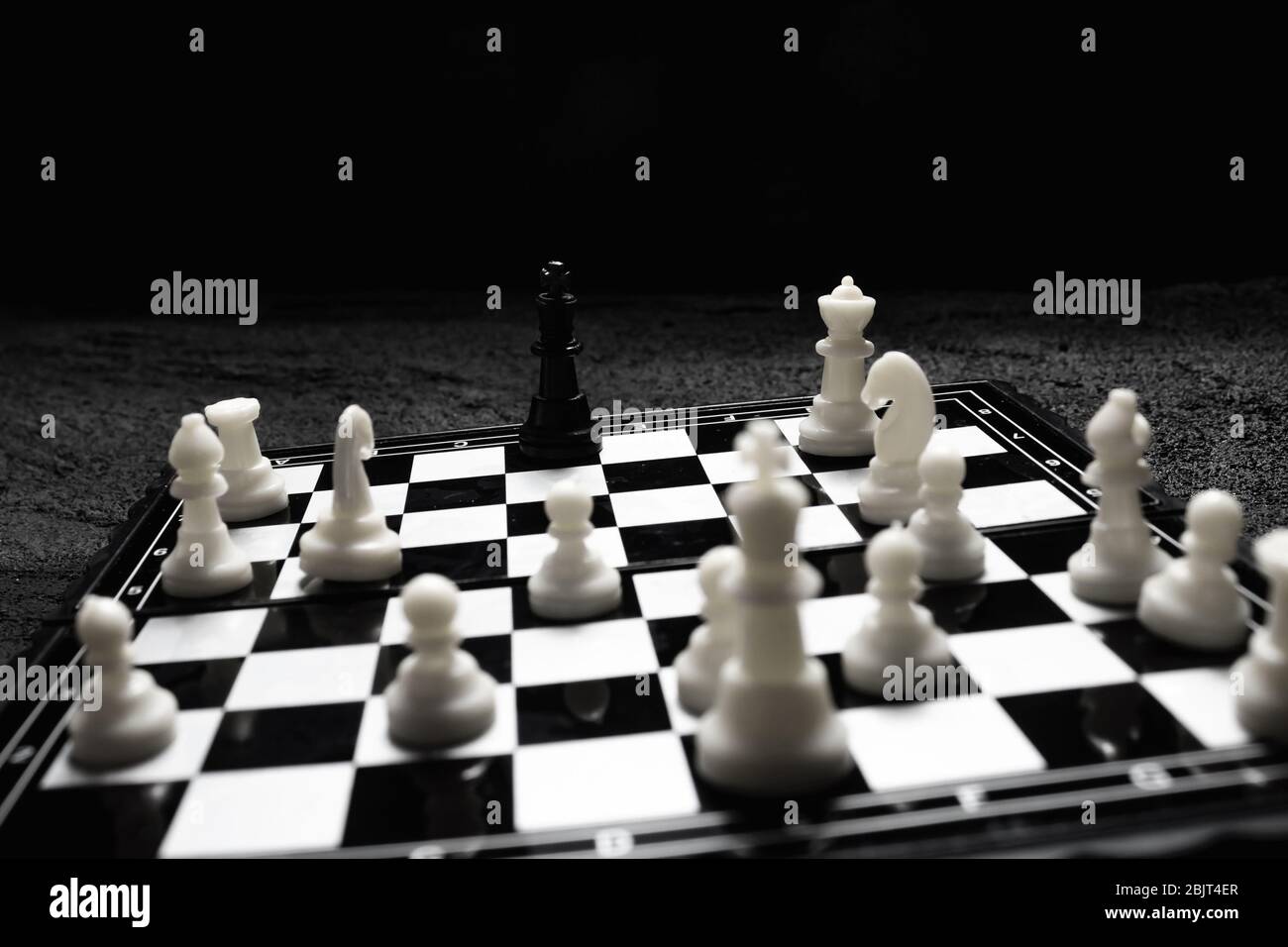 chessboard black king surrounded by enemies ambush on black concrete dark background .copy space Stock Photo