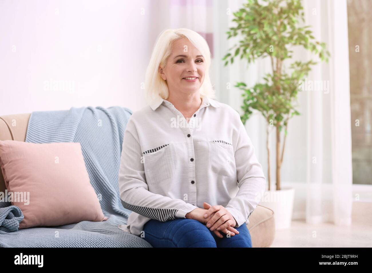 Attractive mature woman sitting on sofa at home Stock Photo - Alamy