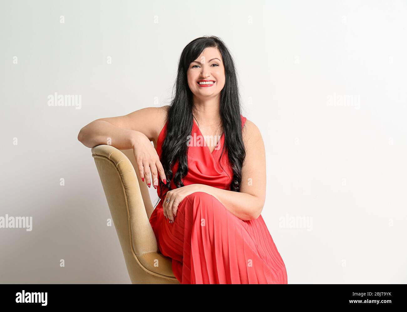 Portrait of attractive mature woman sitting in armchair on white ...