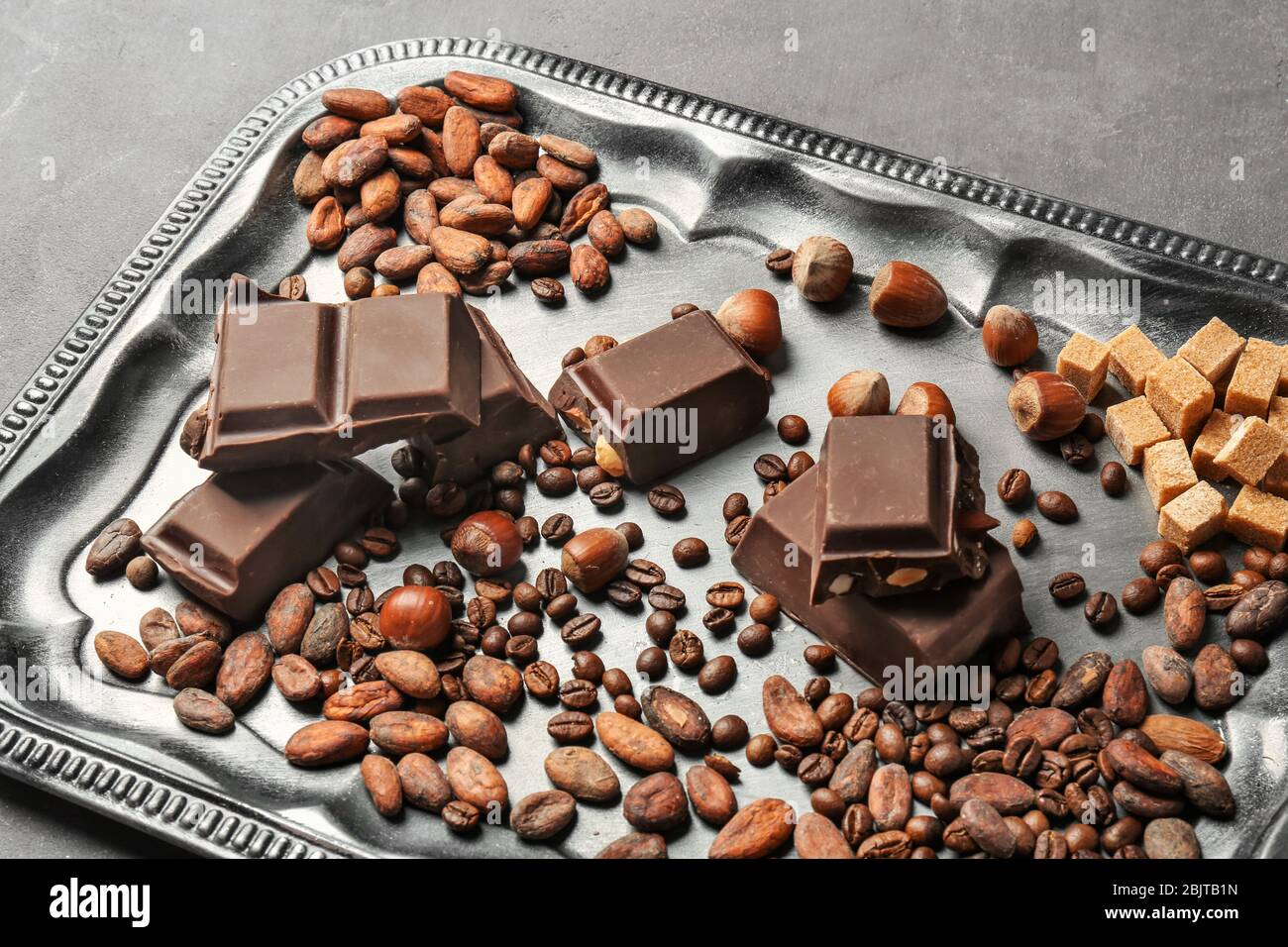 Tray with chocolate, hazelnuts, cocoa and coffee beans on table Stock Photo
