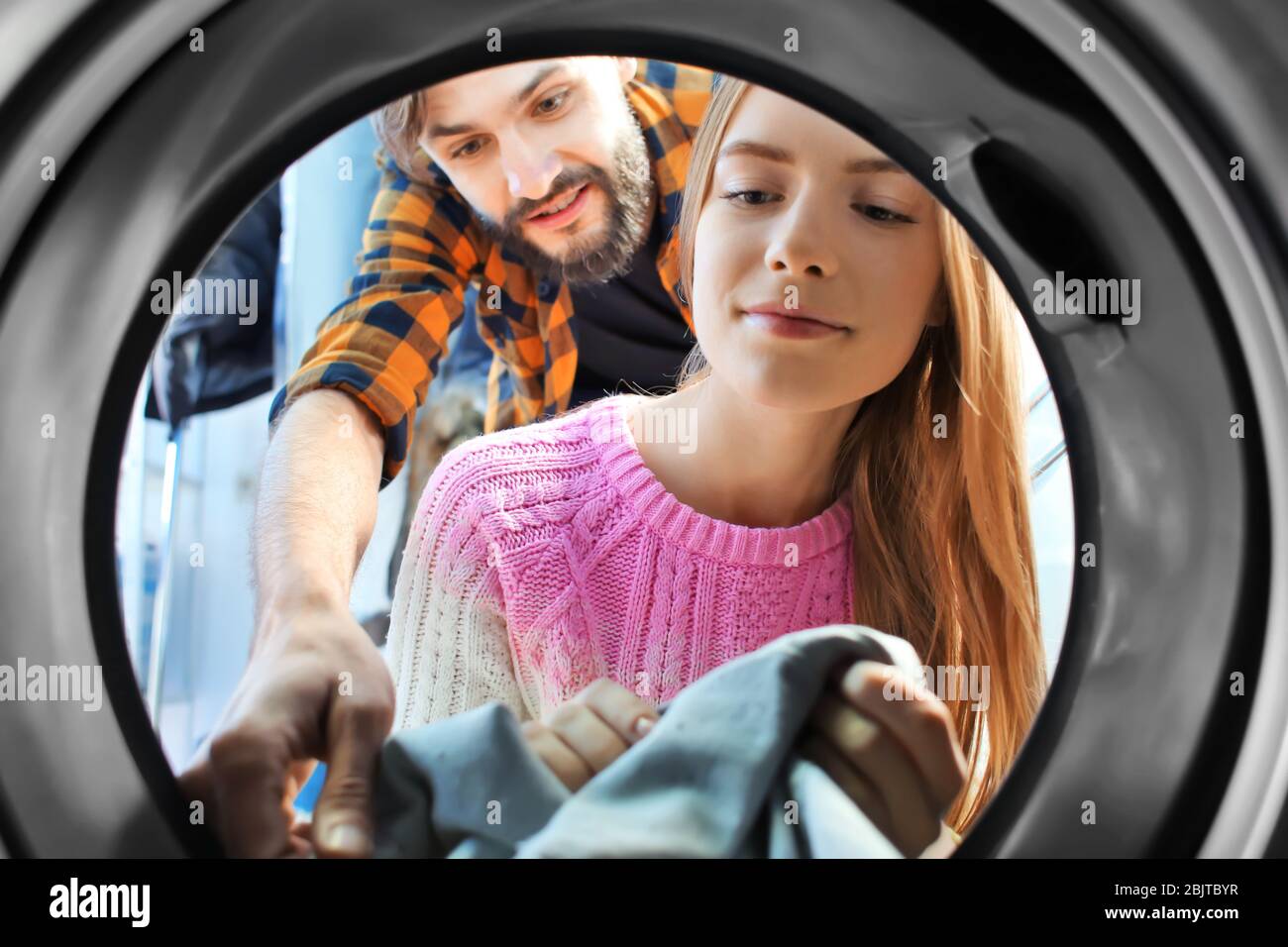 Couple doing laundry in laundromat, view from the inside of washing