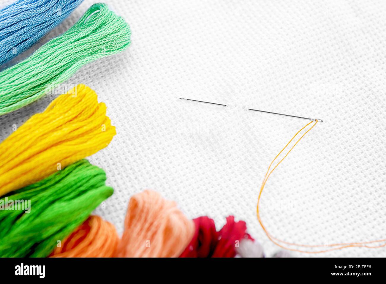 White fabric with colorful threads and sewing needle, closeup Stock Photo