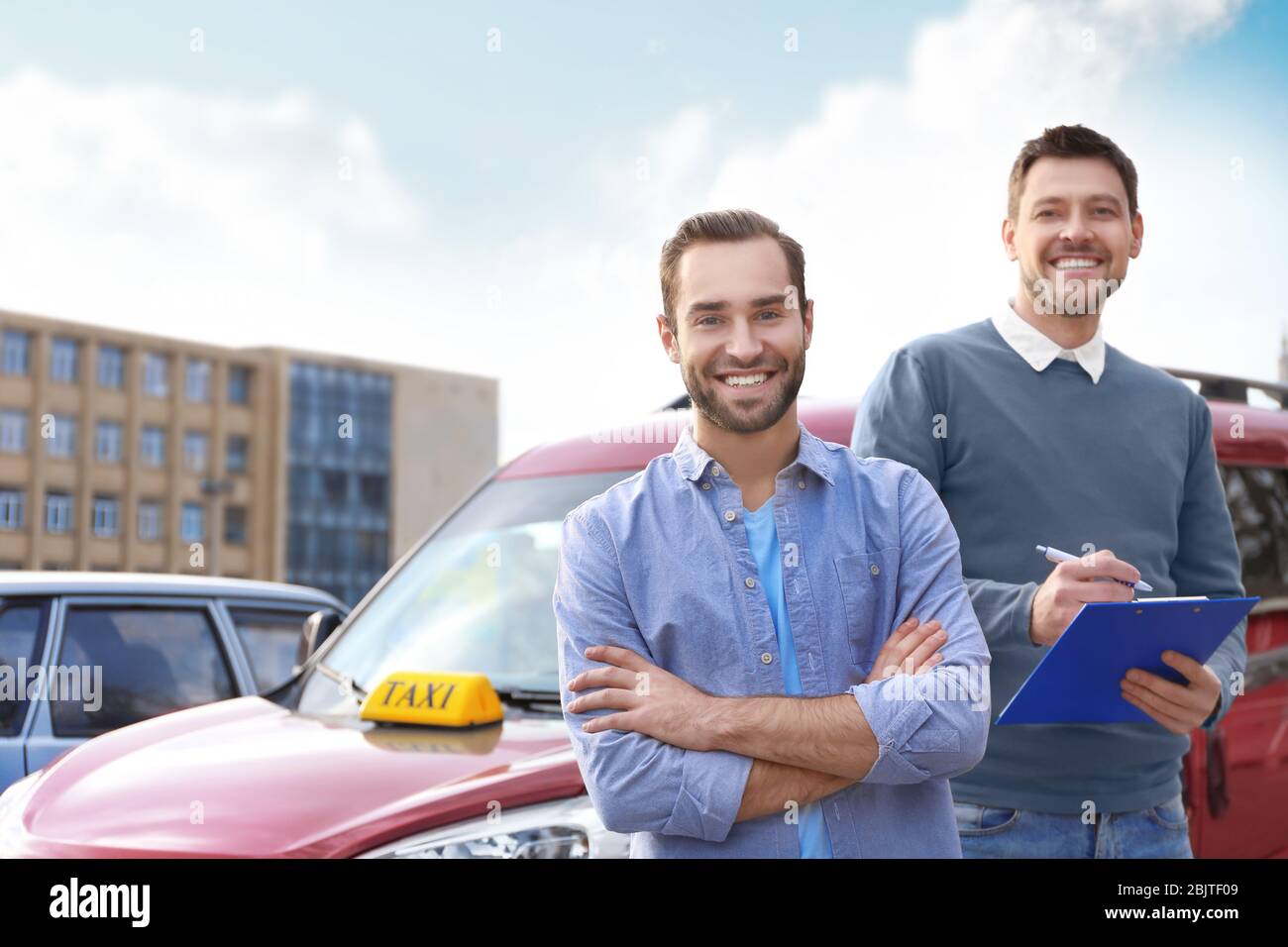 Trainee and driving instructor standing near taxi car outdoors Stock