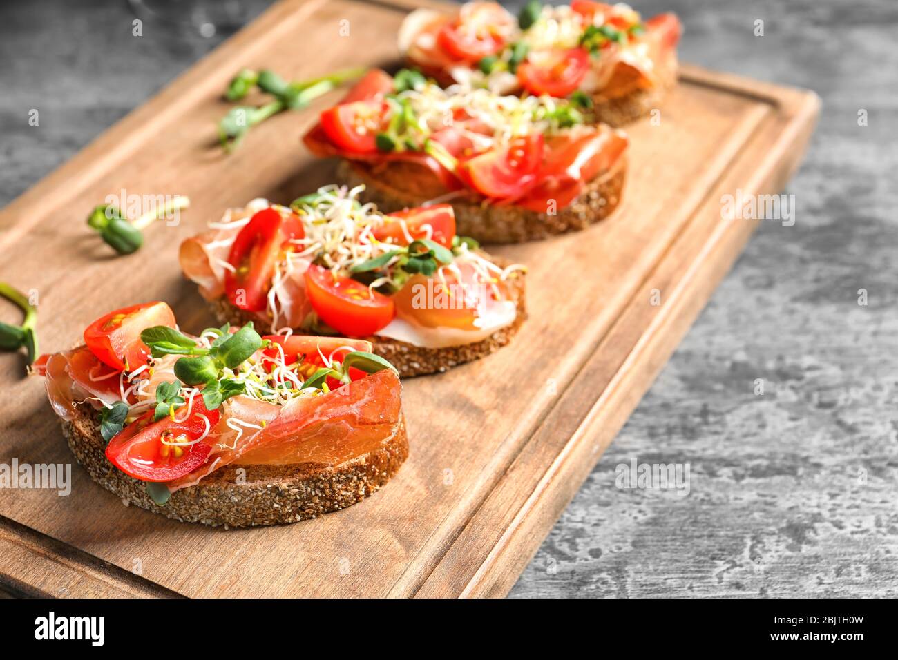 Delicious bruschettas with prosciutto and tomato on wooden board Stock Photo