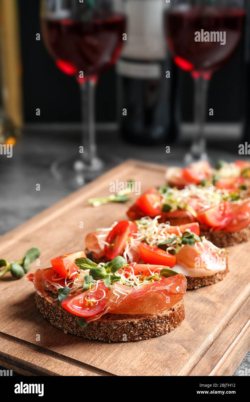 Delicious bruschettas with prosciutto and tomato on wooden board Stock Photo