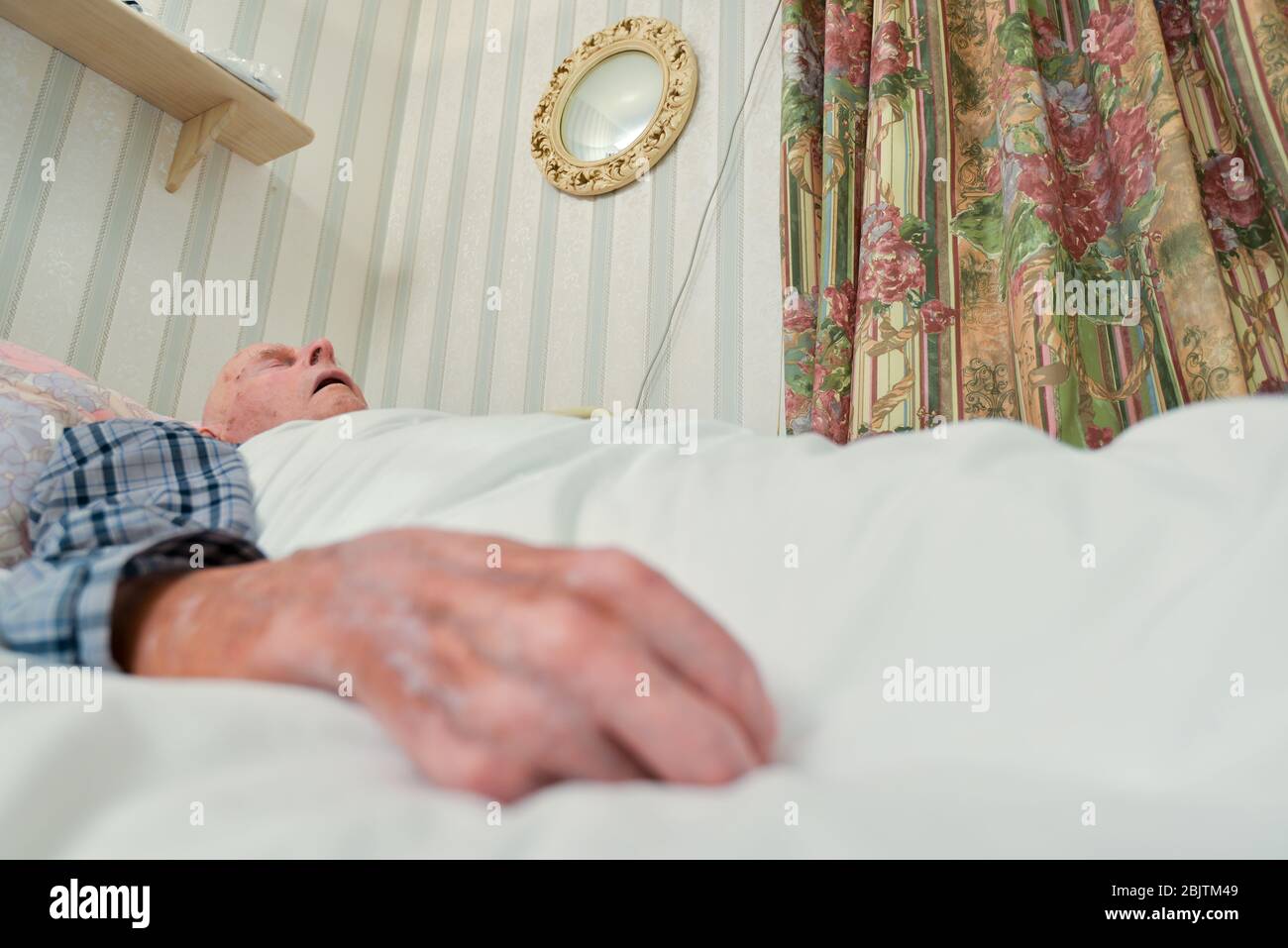 Covered with a duvet,wearing pyjamas in a hospital bed downstairs at his home. Stock Photo