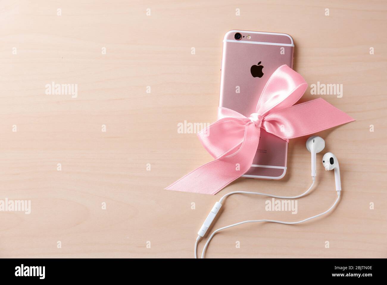 KYIV, UKRAINE - NOVEMBER 28, 2017: Modern iPhone 6s Plus Rose Gold with bow and earpods on wooden background Stock Photo