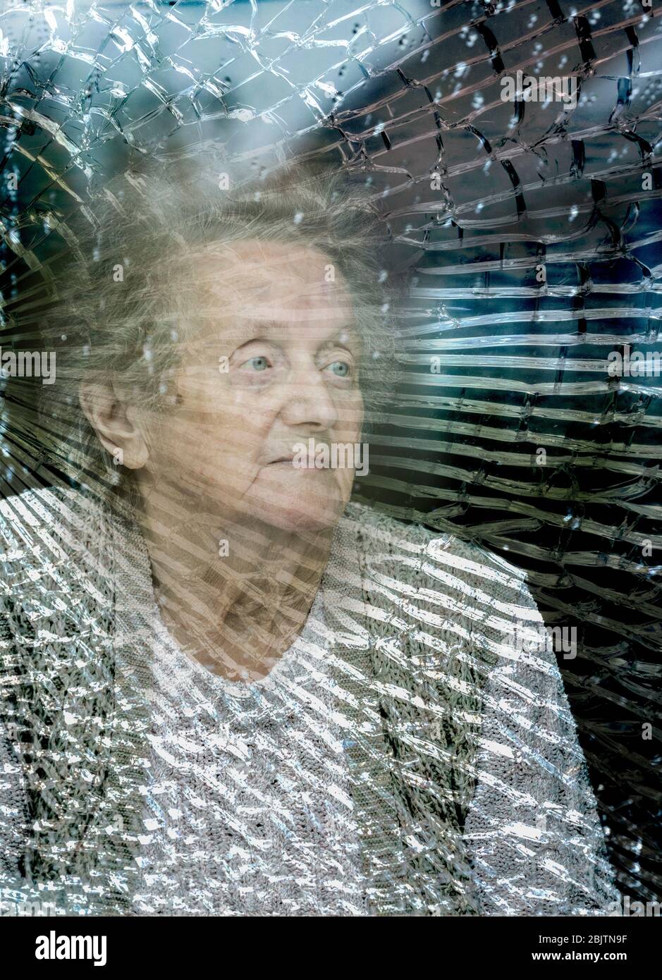 Ninety year old woman looking out of cracked window on a rainy day. Self isolation, loneliness, coronaviurus, social distancing concept... Stock Photo