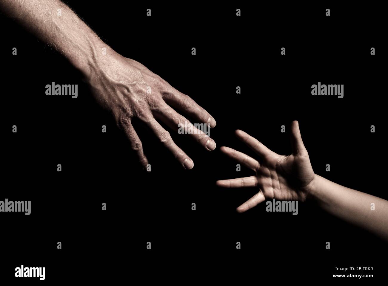Hands reaching out to each other on dark black background Stock Photo