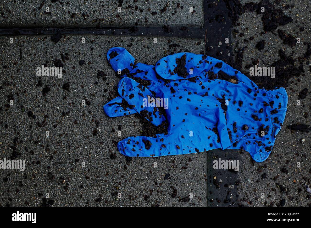 looking down at discarded blue latex glove with fingers crossed, on the sidewalk Stock Photo
