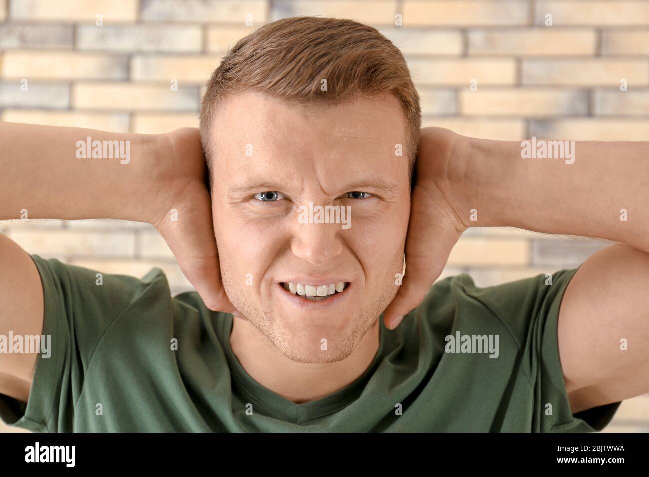 Man covering his ears on brick wall background. Hearing problem Stock ...