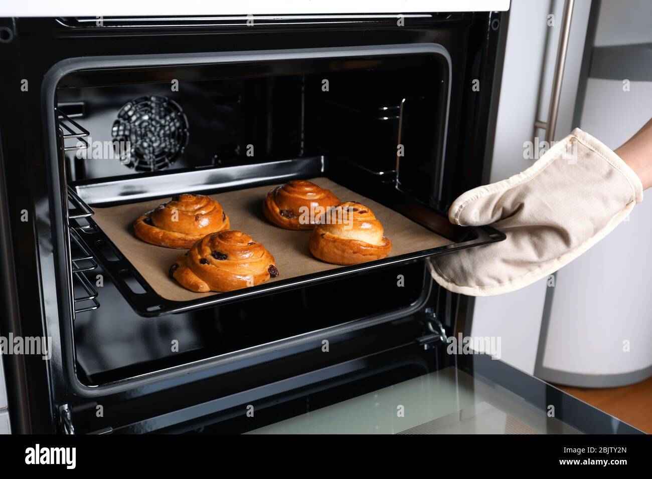 Woman taking baking sheet with buns from oven, closeup Stock Photo - Alamy