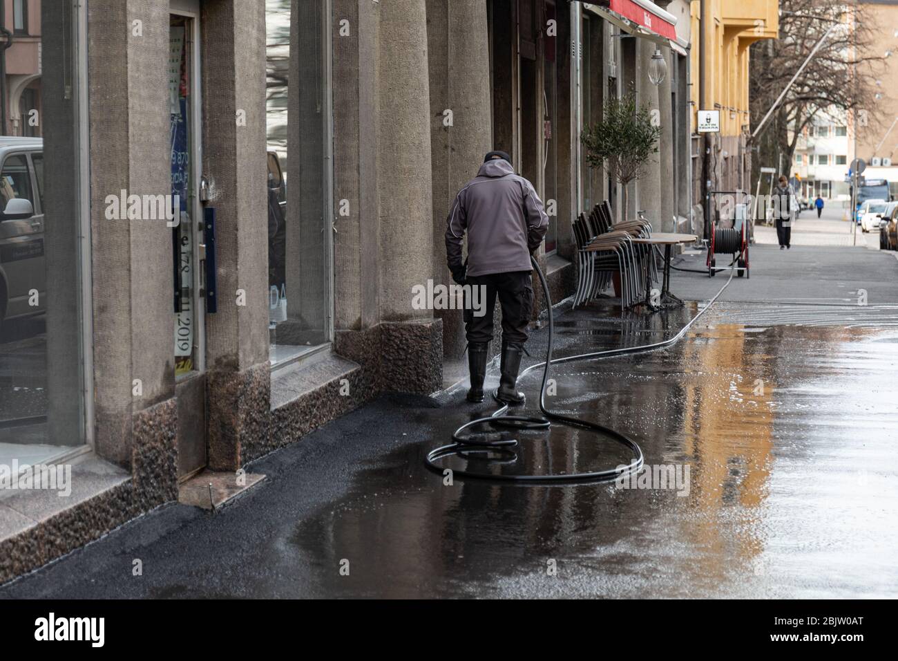 Man in rubber boots hosing down sidewalk in Kallio district of Helsinki, Finland Stock Photo