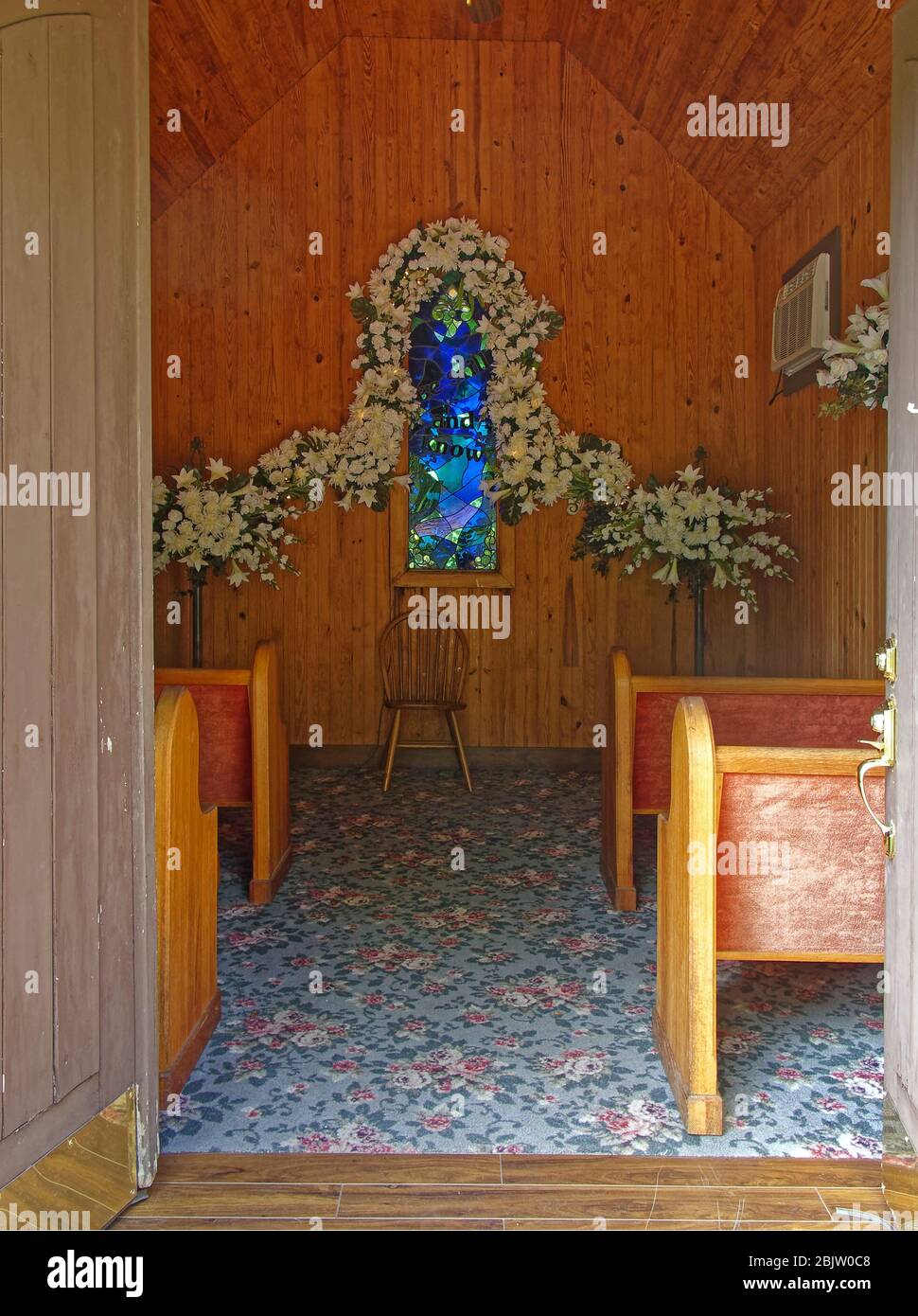 tiny chapel, interior, flower garland, stained glass window, 4 wood pews, wood paneling, flowered carpet, doors open, wedding venue, USA, KY, Kentucky Stock Photo