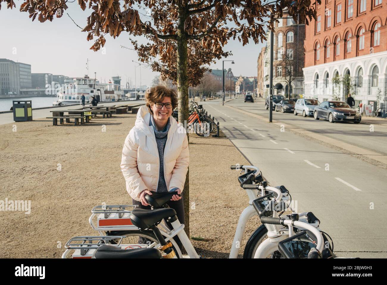 Happy woman renting bicycle at public urban cycle transport station in Copenhagen, Denmark