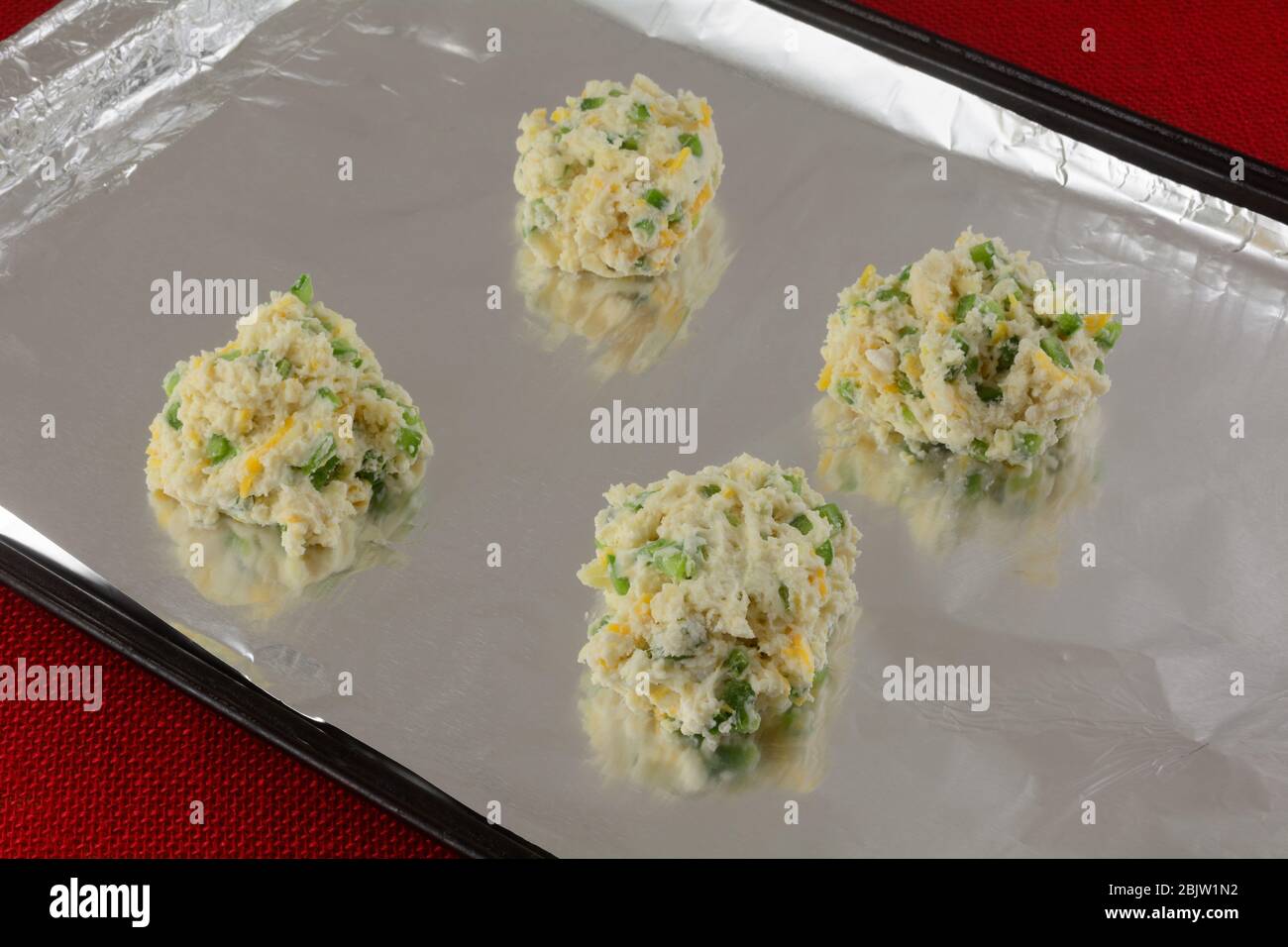 Four raw cheese biscuits with jalapenos on aluminum foil on balking sheet ready for baking Stock Photo