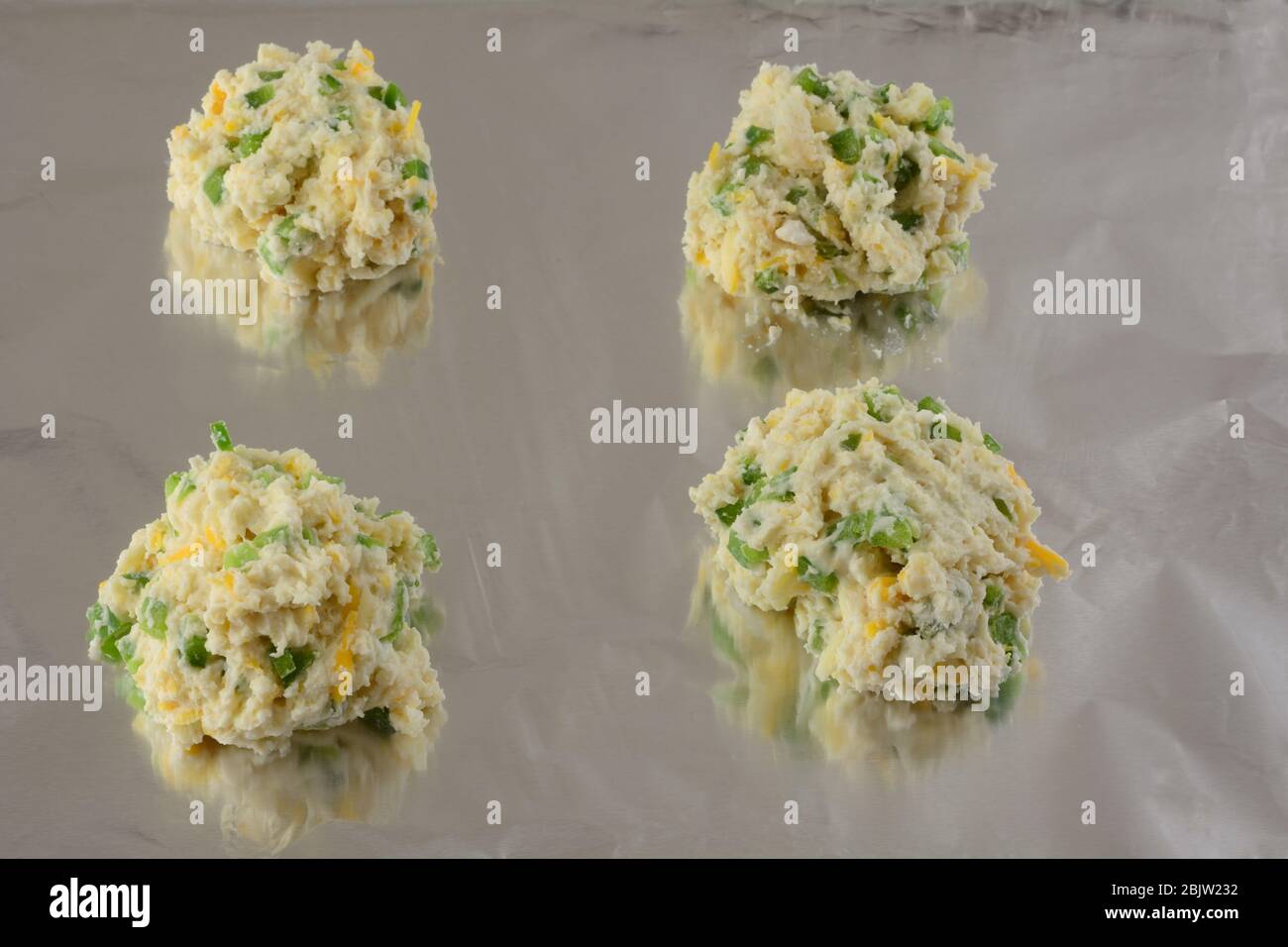 Four raw cheese biscuits with jalapenos on aluminum foil ready for