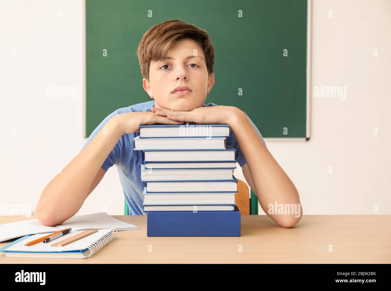 Cute teenager boy with lot of homework to do in classroom Stock Photo ...