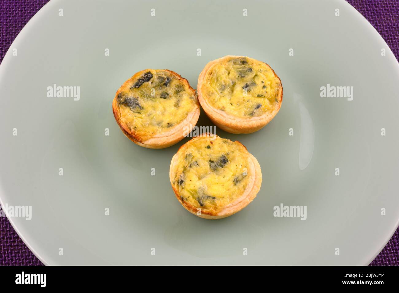 Three mini bite size spinach florentine quiche pastries on green plate Stock Photo