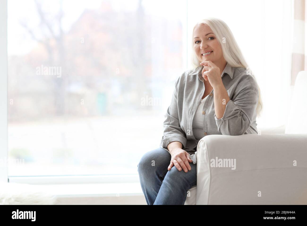 Portrait of beautiful mature woman sitting in armchair at home Stock ...