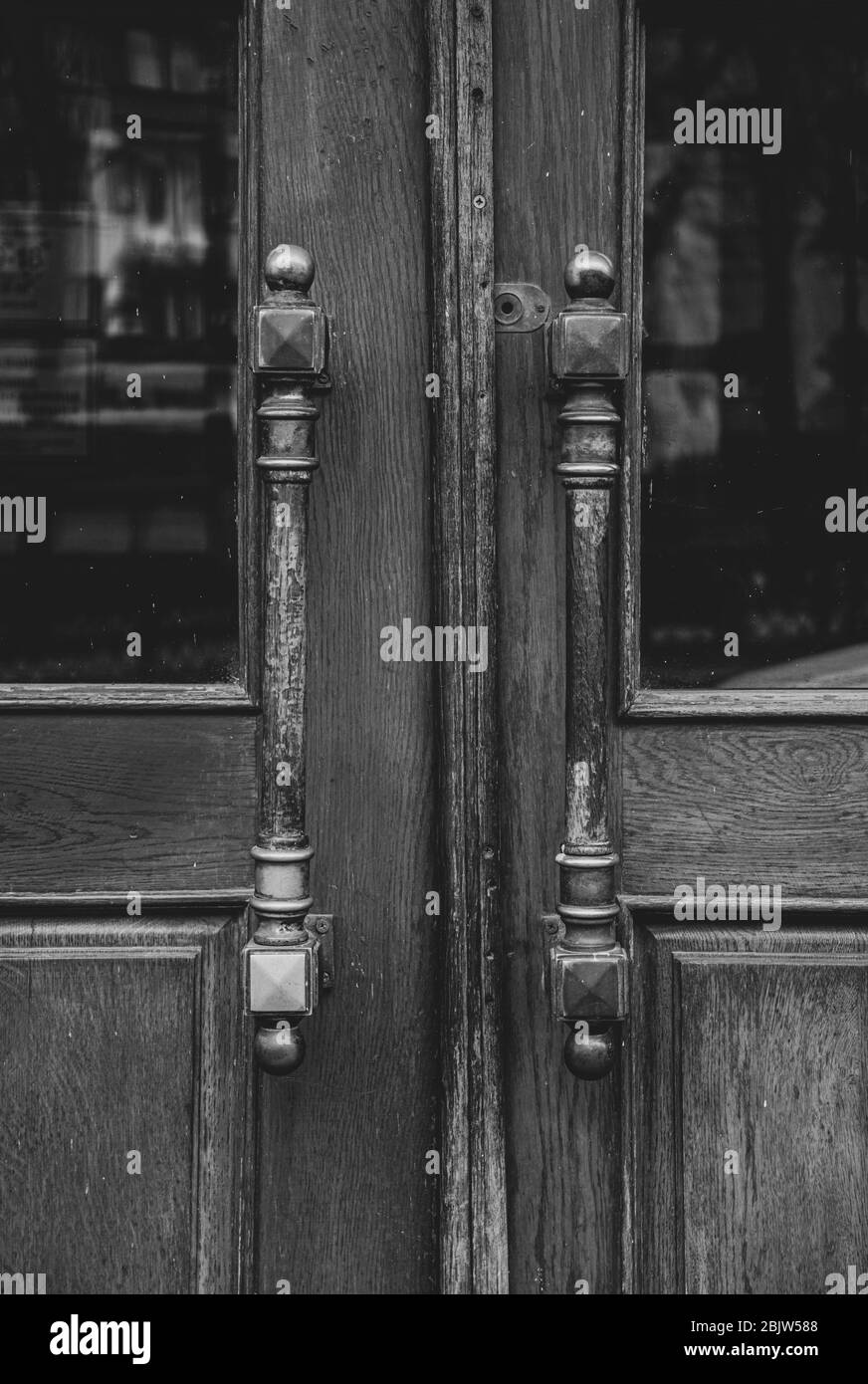 Black and white photo of vintage ornate metal door handles of wooden double door in European city. Symmetric handles and wood texture of old door with Stock Photo