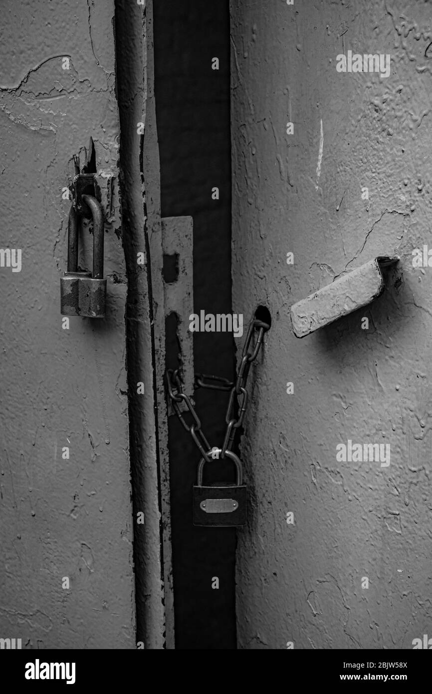 Black and white photo of retro padlocks on rusty chains closed old metal gates painted in grey color. Rough texture of old metal handle and uneven sur Stock Photo