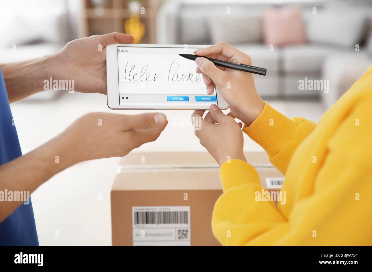 Woman appending signature after receiving parcel from courier indoors Stock Photo