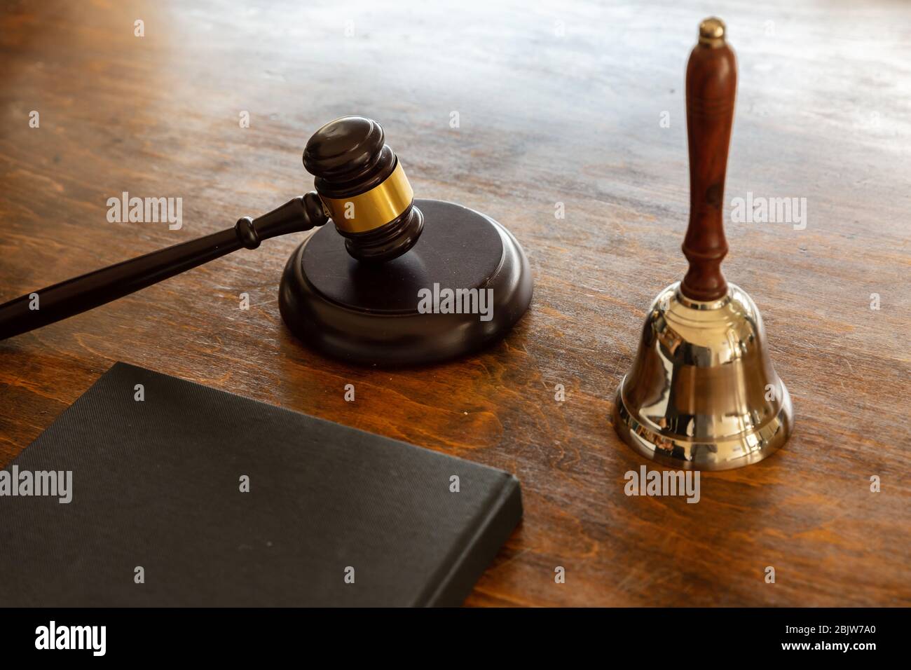 Law theme. Judge gavel and bell, a black blank legal book on wooden desk background, copy space. Auction, court table Stock Photo