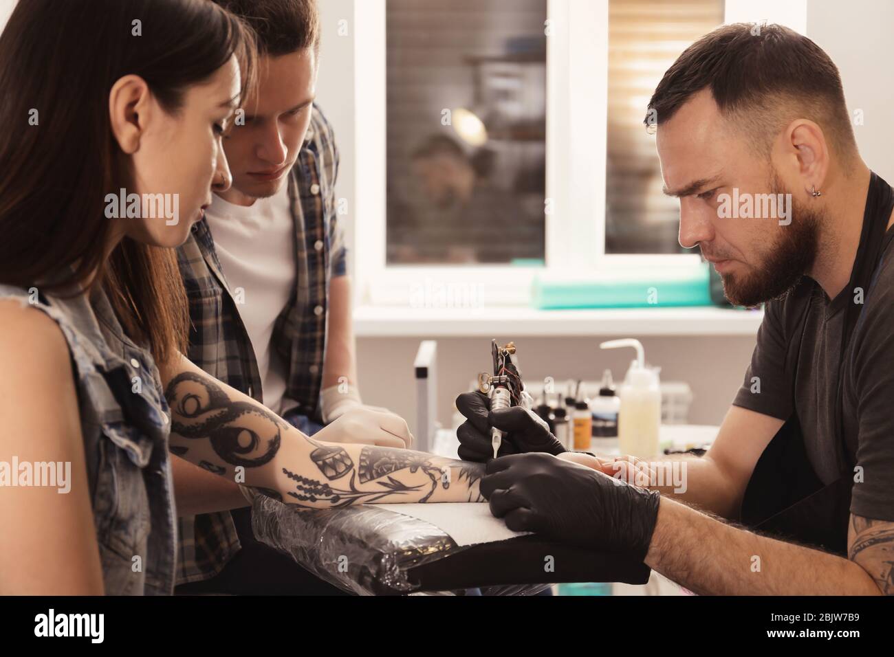 Professional tattoo master teaching young specialist in salon