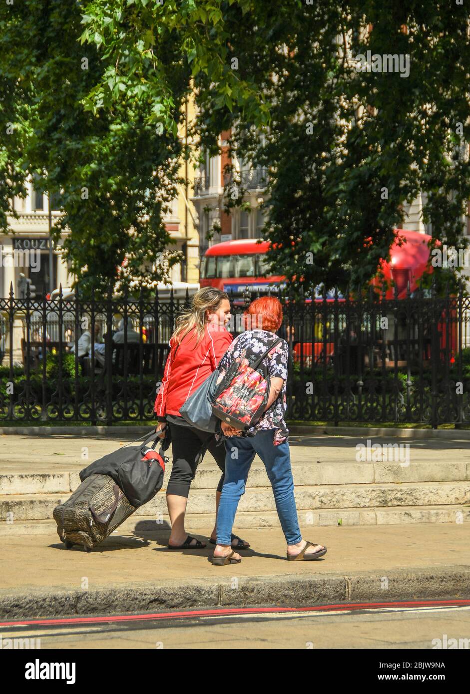 LONDON, ENGLAND - JULY 2018: Two women walking down a street in central London one of whom is pulling a suitcase Stock Photo