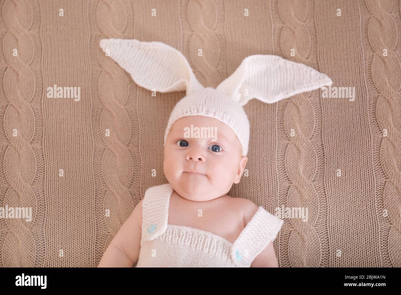 Cute little baby in bunny costume lying on plaid, top view Stock Photo