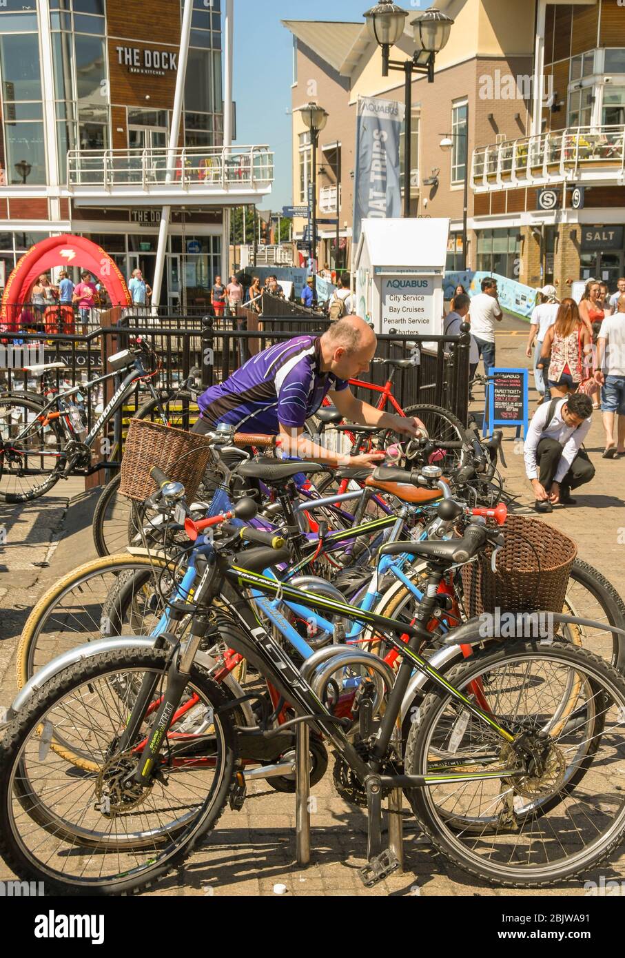 CARDIFF BAY, CARDIFF, WALES - JULY 2018: Cyclist securing his bicycle to a cycle rack with other bikes in Cardiff Bay Stock Photo