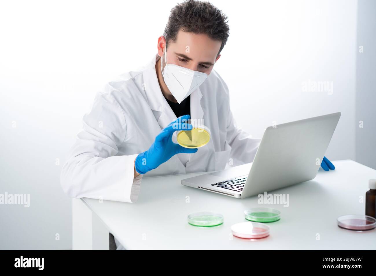 Young Male researcher or Scientist examining solution in petri dish at a laboratory. The researcher is analyzing the medicine related innovation. Bioc Stock Photo