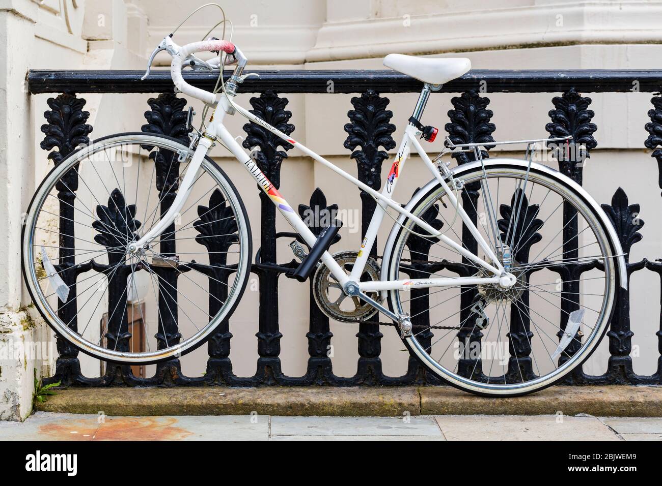 A ladies white Raleigh bicycle padlocked to a set of railings, UK Stock Photo