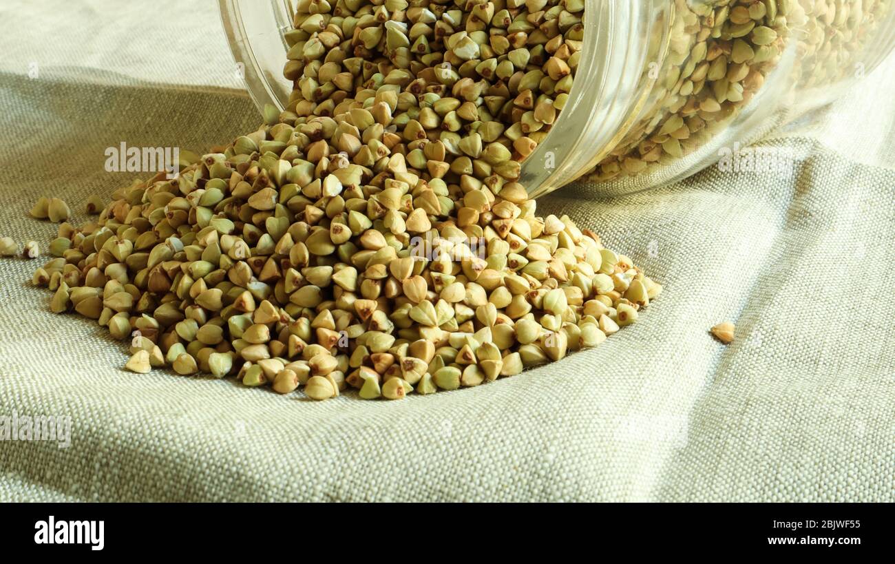 Scattered raw green buckwheat with a glass jar for cereals. Vegan