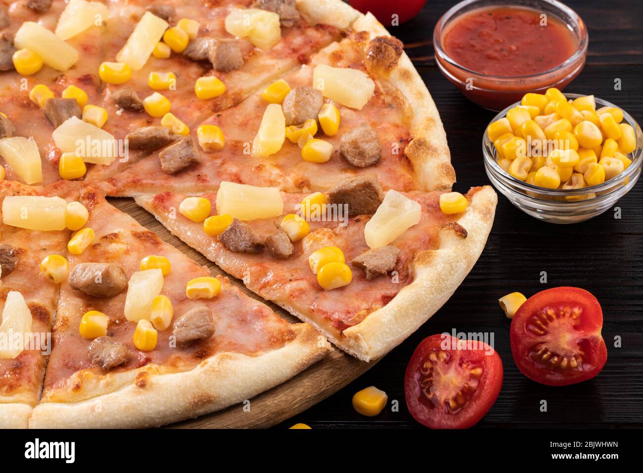 Pizza with chicken, pineapple and corn on dark background. Stock Photo