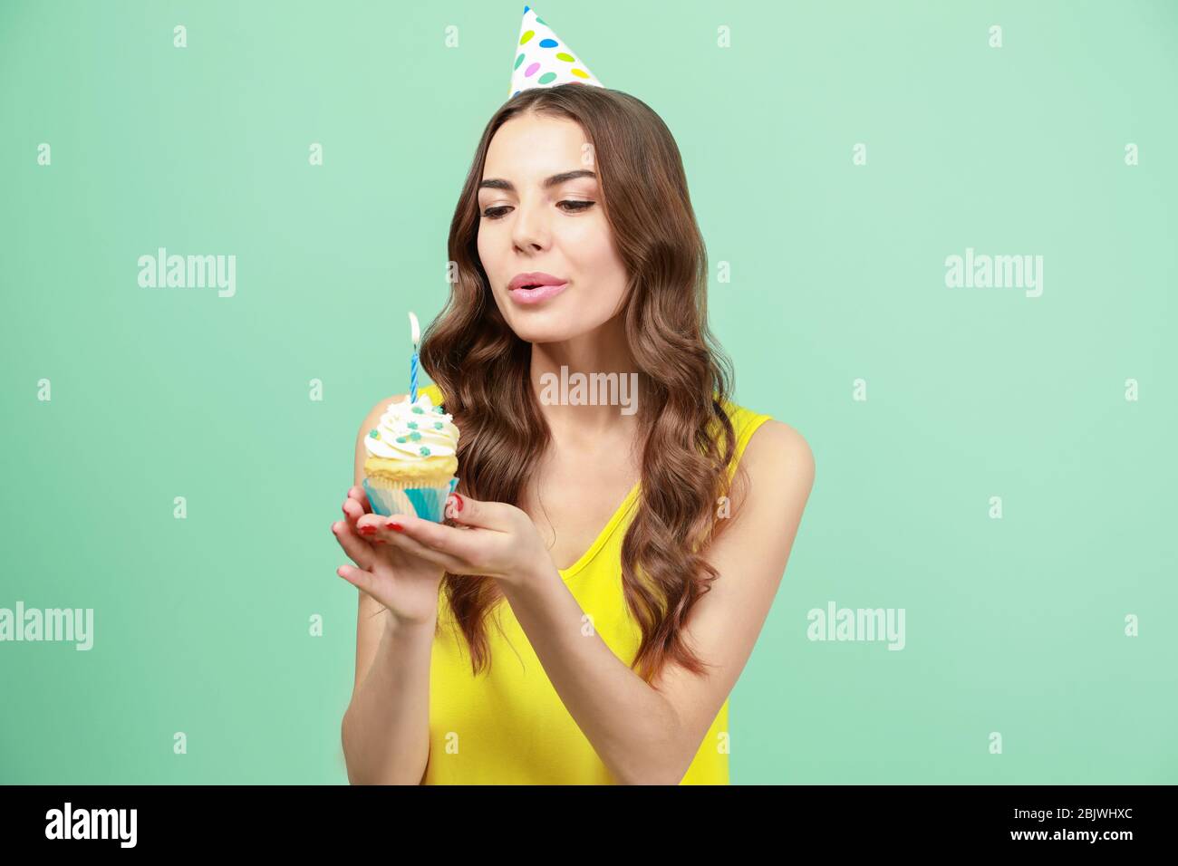Beautiful young woman snuffing out candle on birthday cupcake against