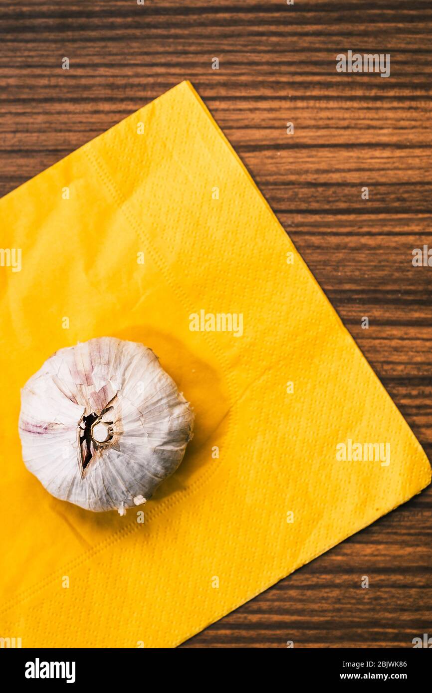 Garlic head on a yellow napkin and a traditional vintage-style wooden countertop. Preparing a recipe for garlic cooking. Stock Photo