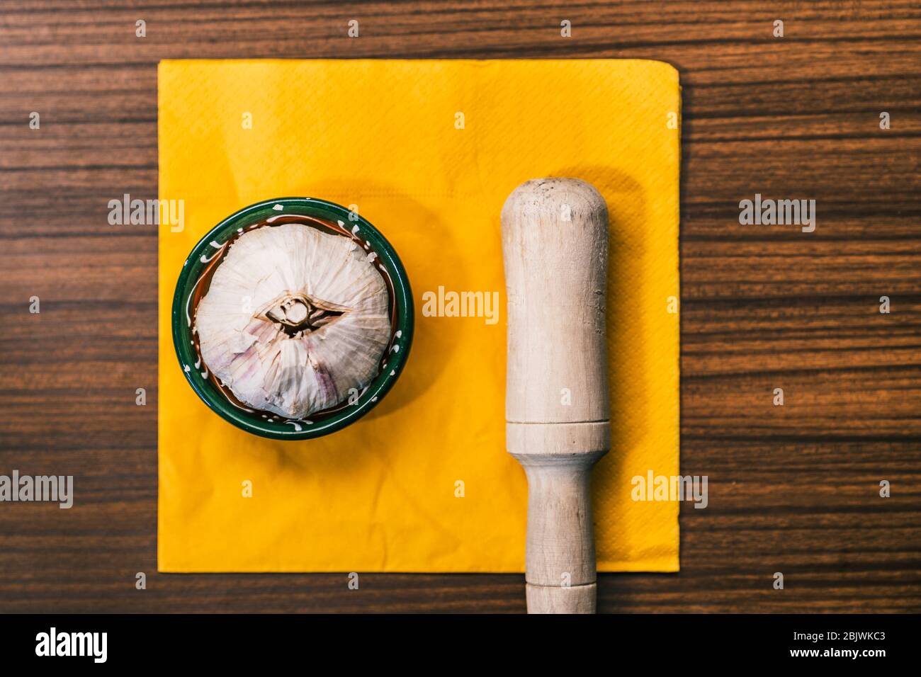 Garlic head next to a hand of mortar on top of a traditional style wooden countertop. Preparing a garlic recipe for making aioli. Stock Photo