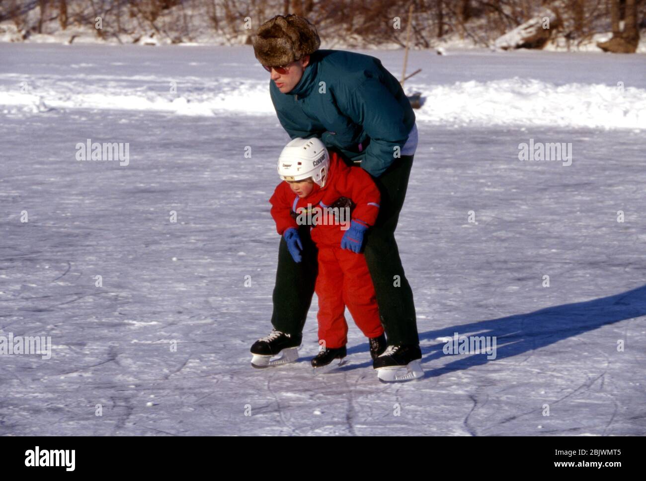 A father helps his young son skate on an outdoor frozen pond Stock Photo