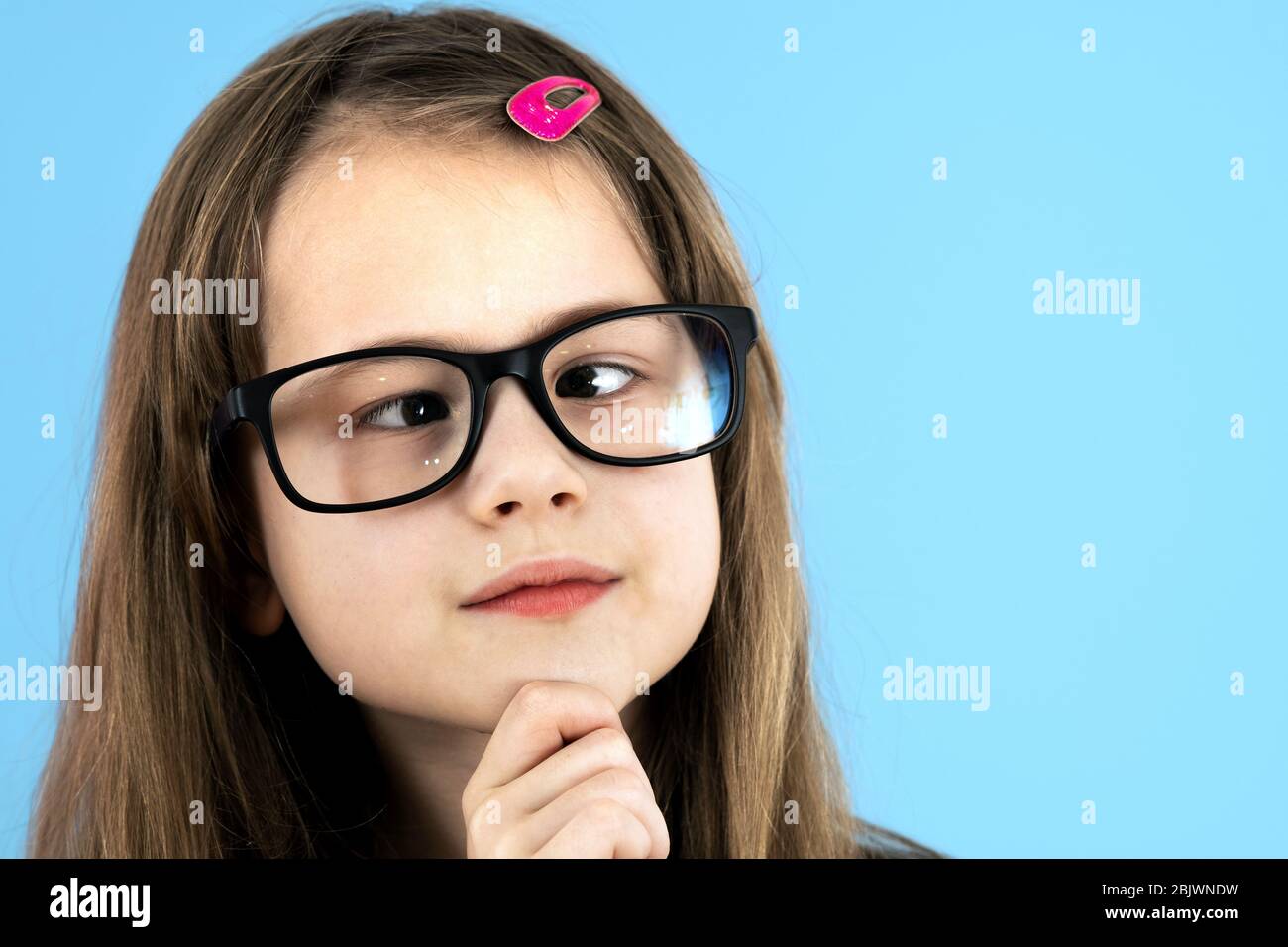 Close up portrait of a cross eyed child school girl wearing looking glasses isolated on blue background. Stock Photo