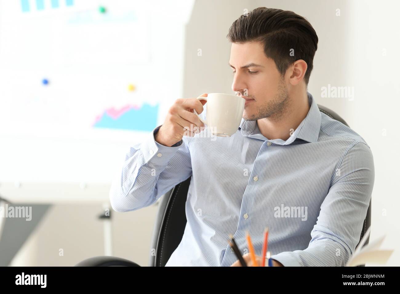 Young man drinking coffee at workplace Stock Photo