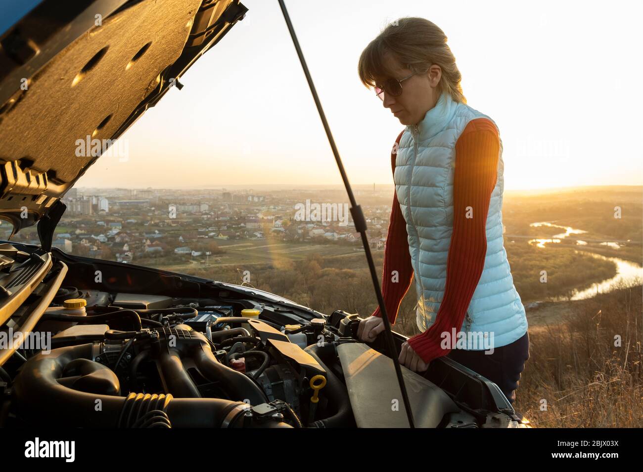 Young woman standing near broken down car with popped up hood having ...